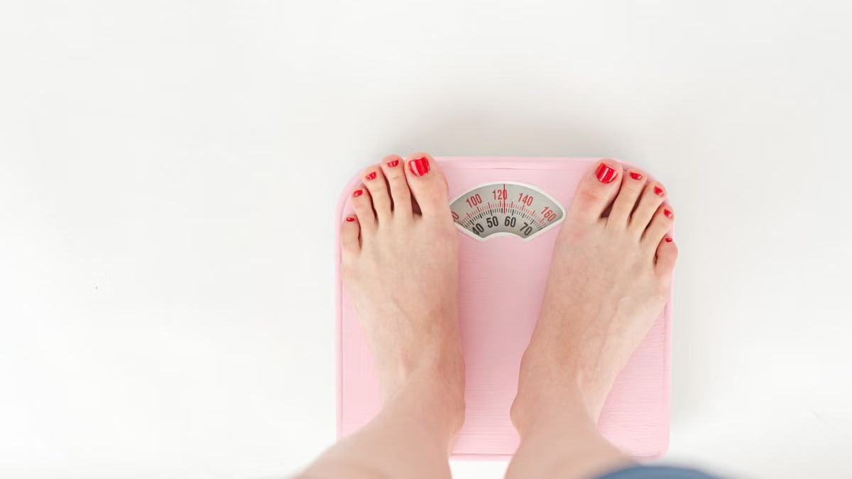 Top view of crop anonymous barefoot female measuring weight on scales on white background